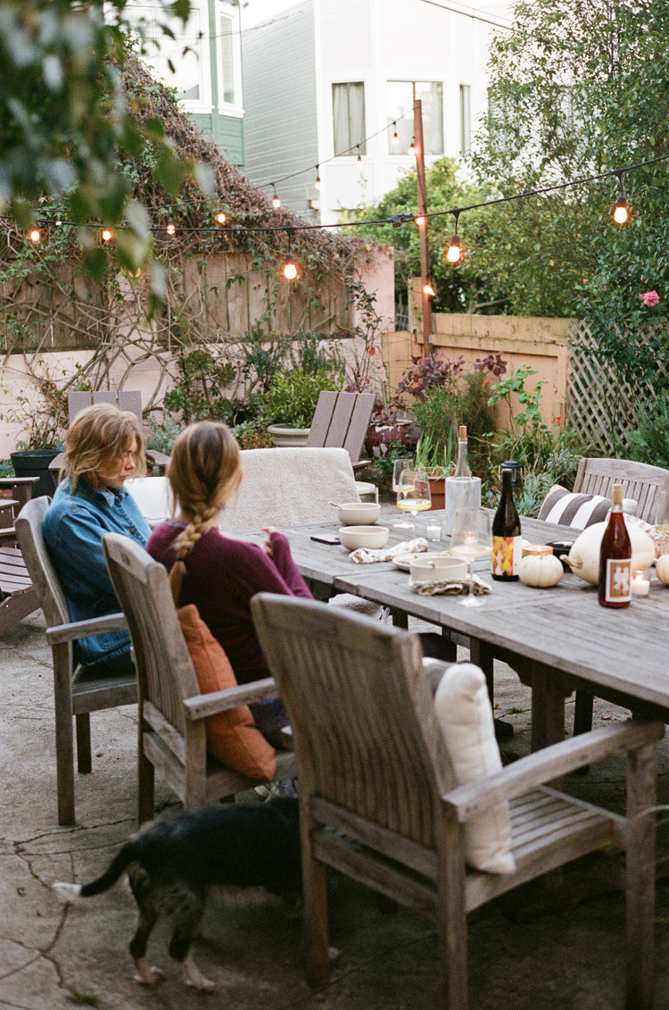 Two people sitting at a table for a meal outside with bottles of wine.