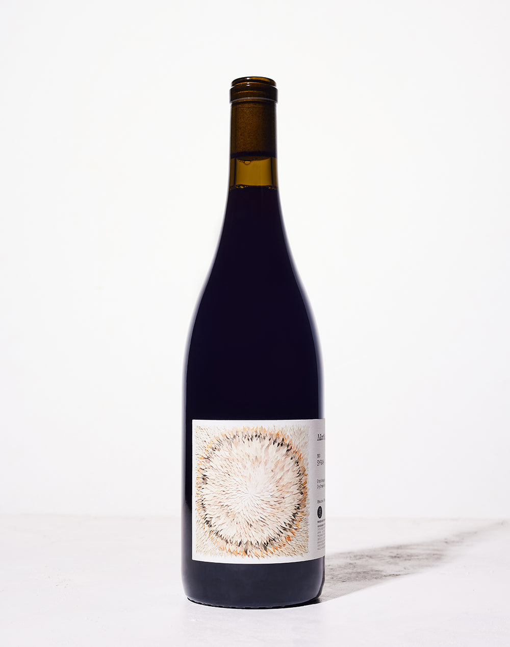 A wine bottle against a white background, featuring a label with an abstract circular pattern of light and dark brown brush strokes. Simple and elegant design.