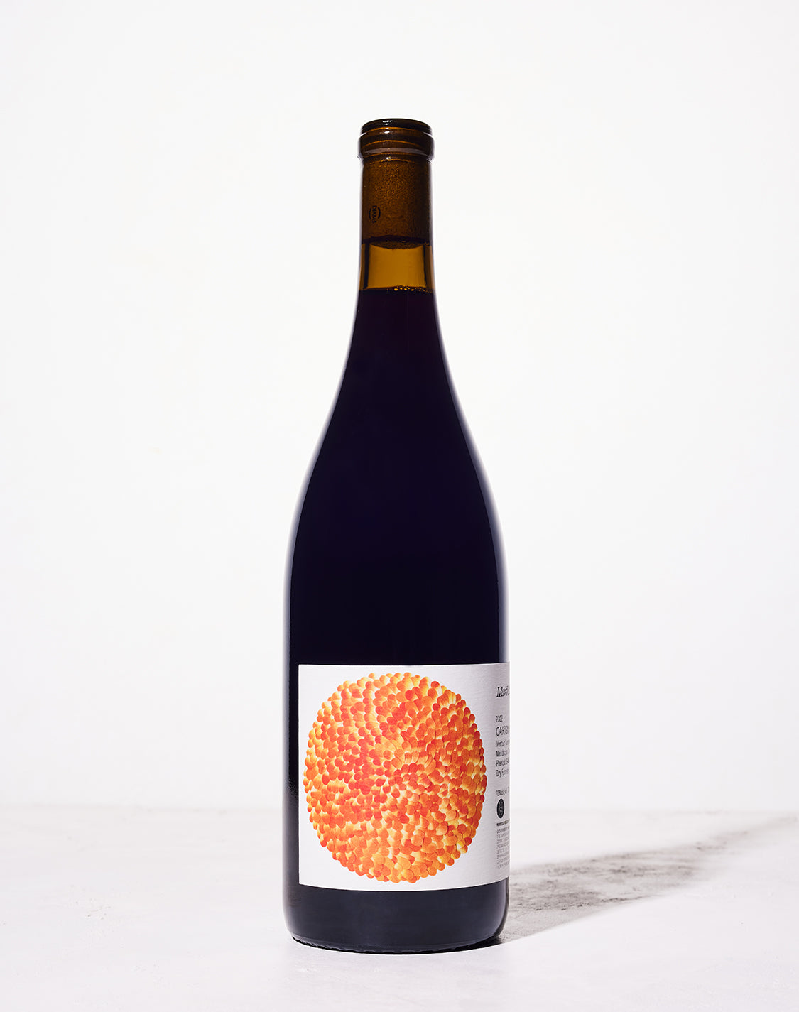 A bottle of wine with a dark glass and an artistic label featuring an orange and yellow textured circular pattern, set against a plain white background.