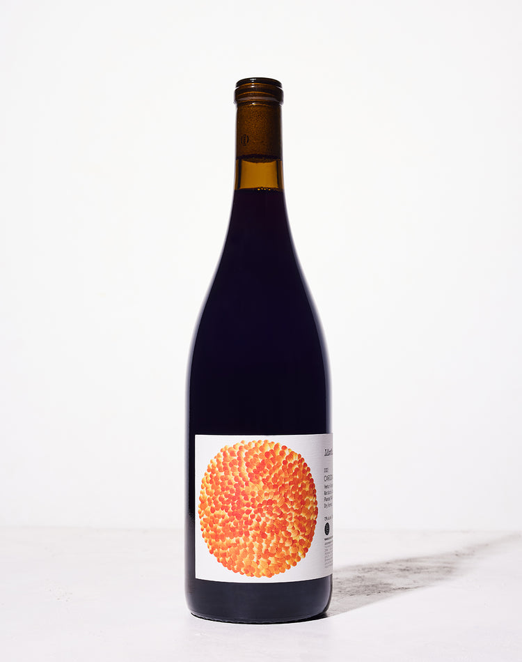 A bottle of wine with a dark glass and an artistic label featuring an orange and yellow textured circular pattern, set against a plain white background.