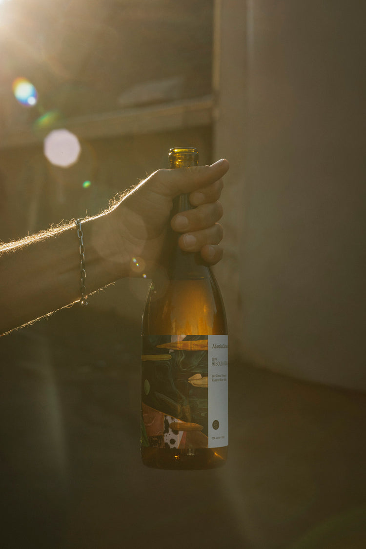 A man's hand holds a bottle of wine in the sunlight, with light flares around it.