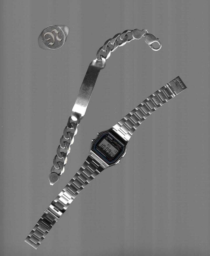 A metallic digital wristwatch with a light display and a stainless steel bracelet lies beside a chunky silver chain bracelet and a metal ring with a logo.