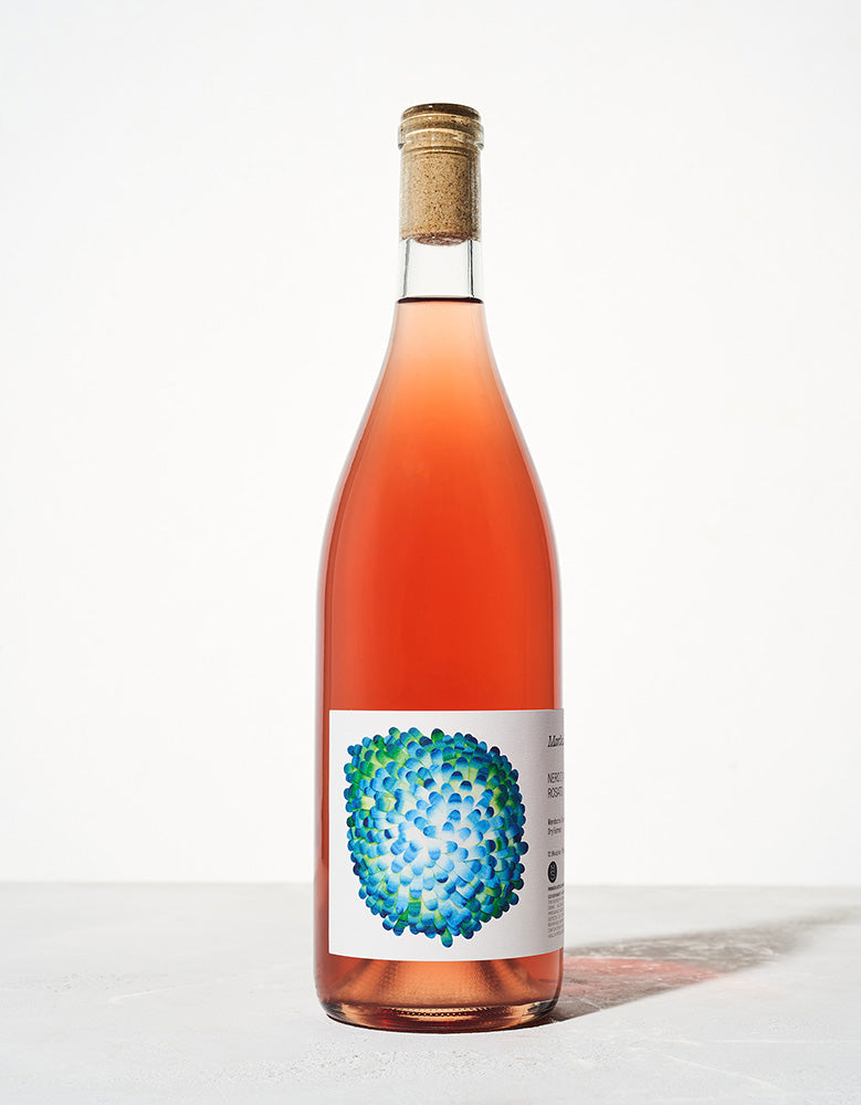 A bottle of rosé wine with a simple cork sits against a white background. The label features vibrant green and blue abstract art, conveying a fresh and modern feel.