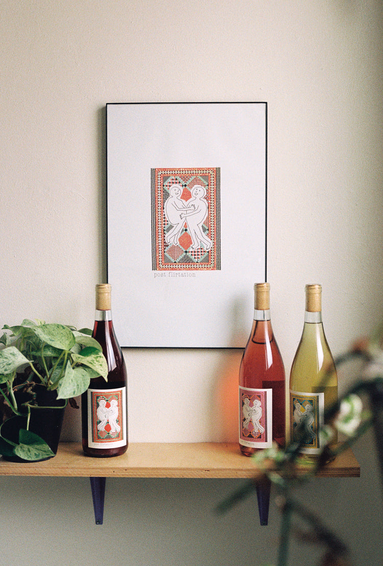 Three wine bottles on a shelf with a Post Flirtation image in a frame handing on a wall.