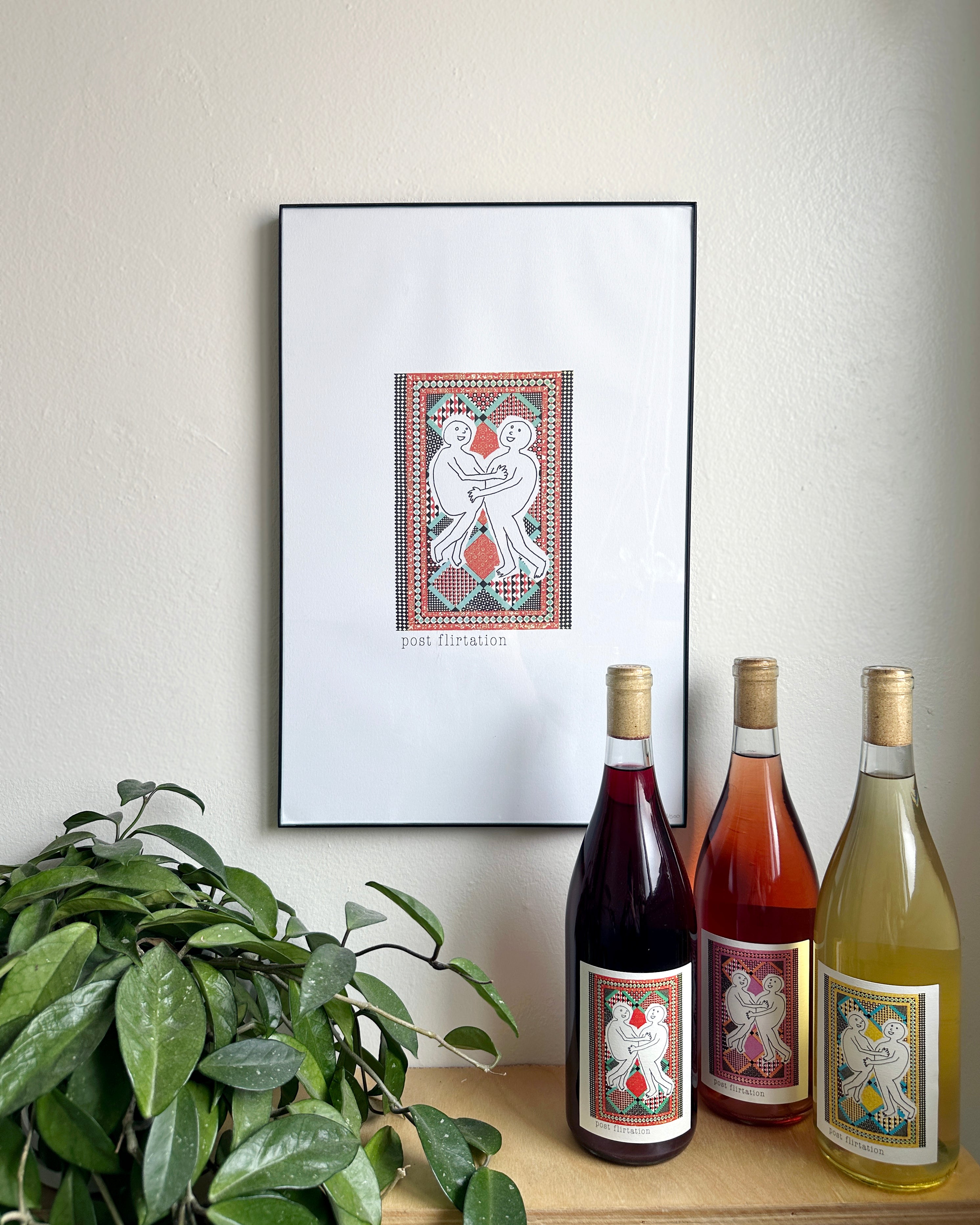 Framed artwork titled "post flirtation" featuring abstract figures on a wall. Below, three wine bottles with similar labels and a leafy plant create a cozy setting.