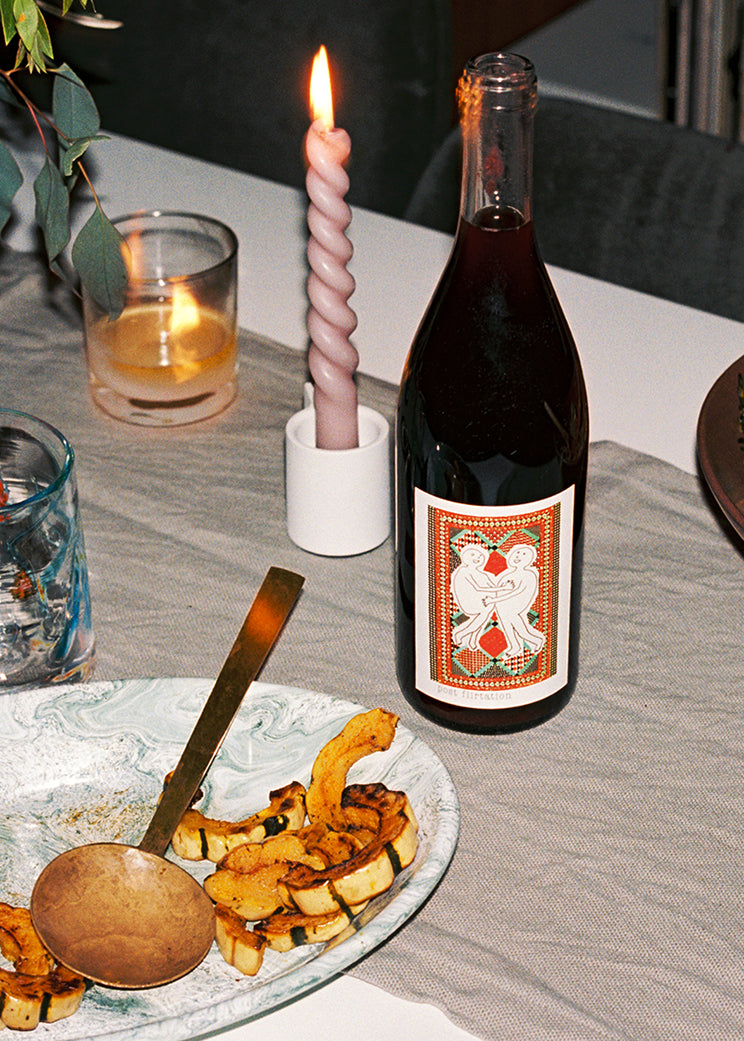 A cozy table setting featuring a bottle of wine, a lit candle, and a plate of sliced squash.