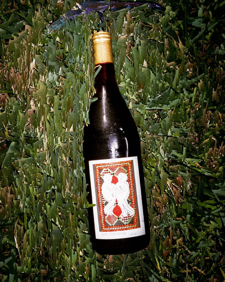 A wine bottle with a decorative label featuring two figures dancing, resting on green grass.