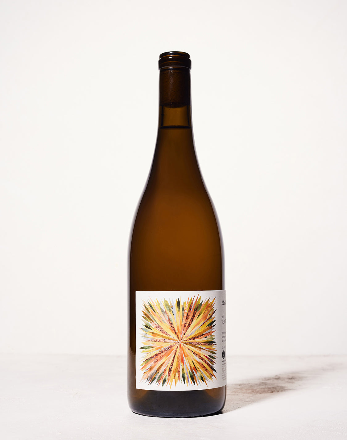 A brown wine bottle stands against a light background. The label features a colorful, sunburst design with vibrant orange, yellow, and green hues.