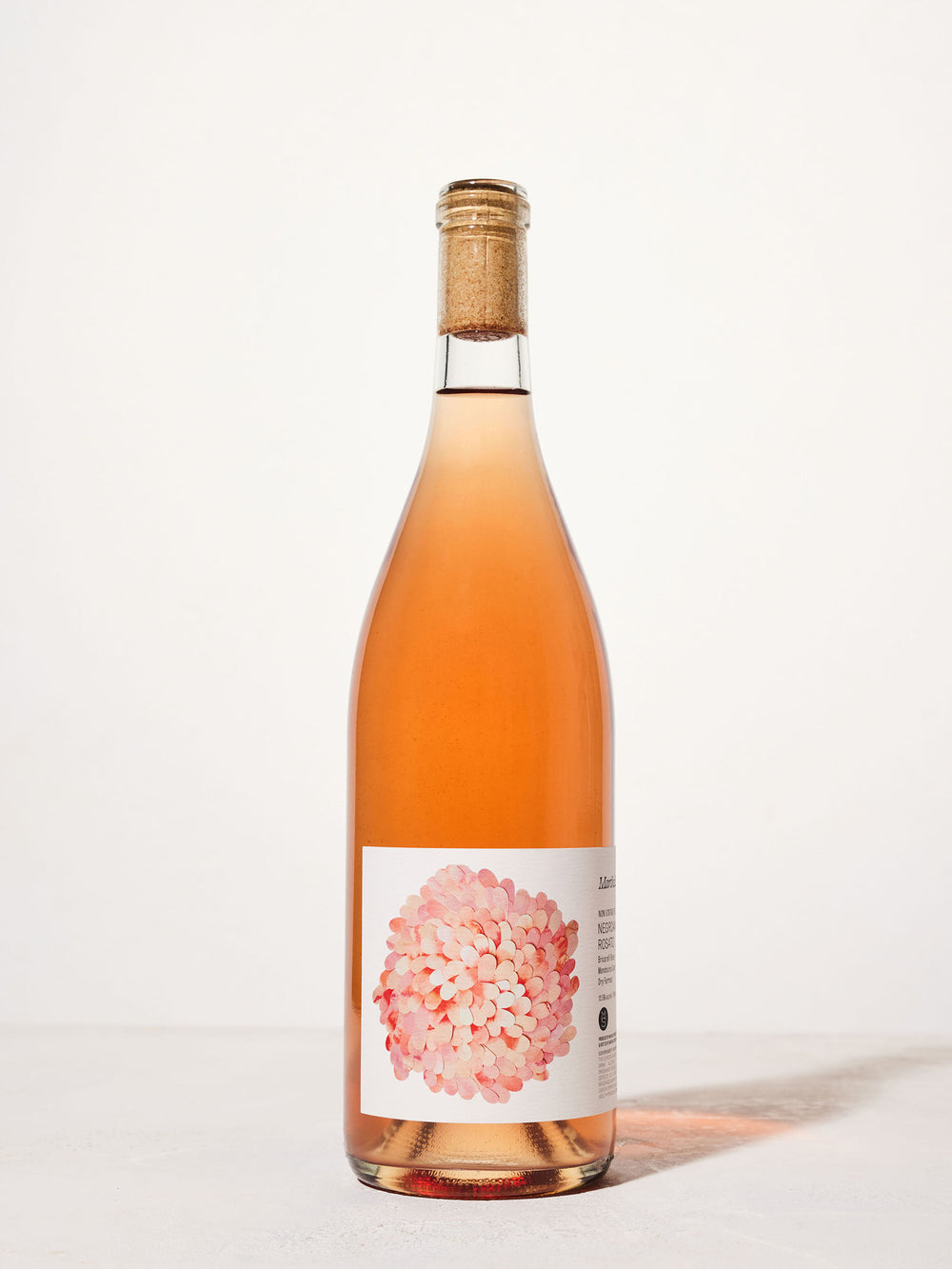 A tall bottle of rosé wine with a cork top stands against a plain white background. The label features a pink and white floral design, creating a fresh and elegant look.