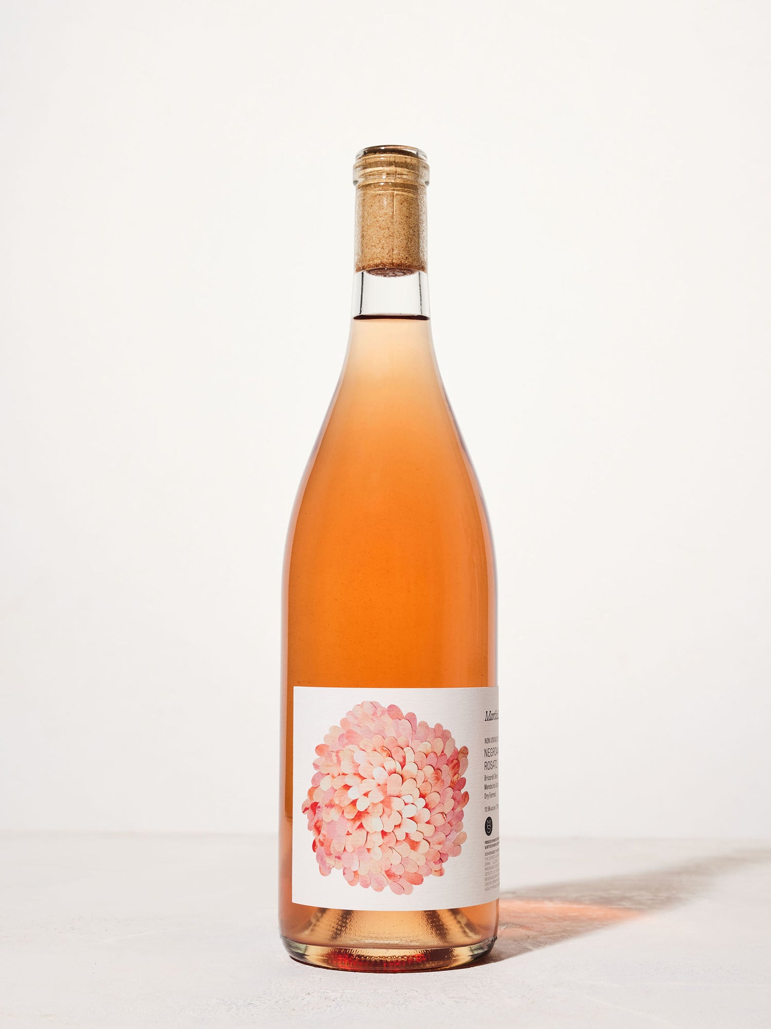 A tall bottle of rosé wine with a cork top stands against a plain white background. The label features a pink and white floral design, creating a fresh and elegant look.