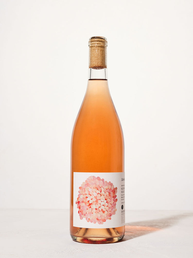 A tall bottle of rosé wine with a cork top stands against a plain white background. The label features a pink and white floral design, creating a fresh and elegant look.