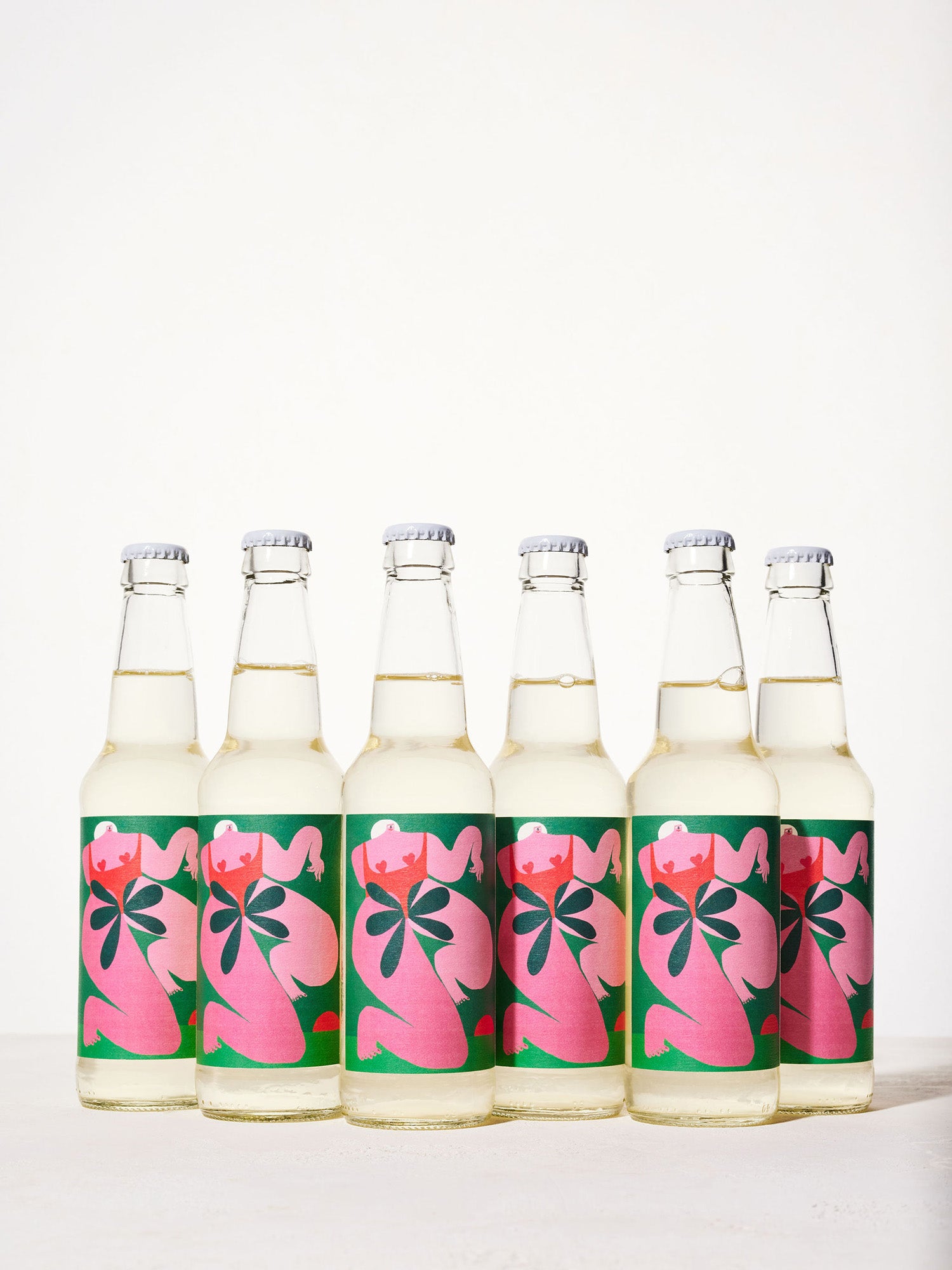 Six green glass bottles with vibrant pink labels featuring abstract floral designs are arranged in a row on a white surface, conveying a fresh and artistic tone.