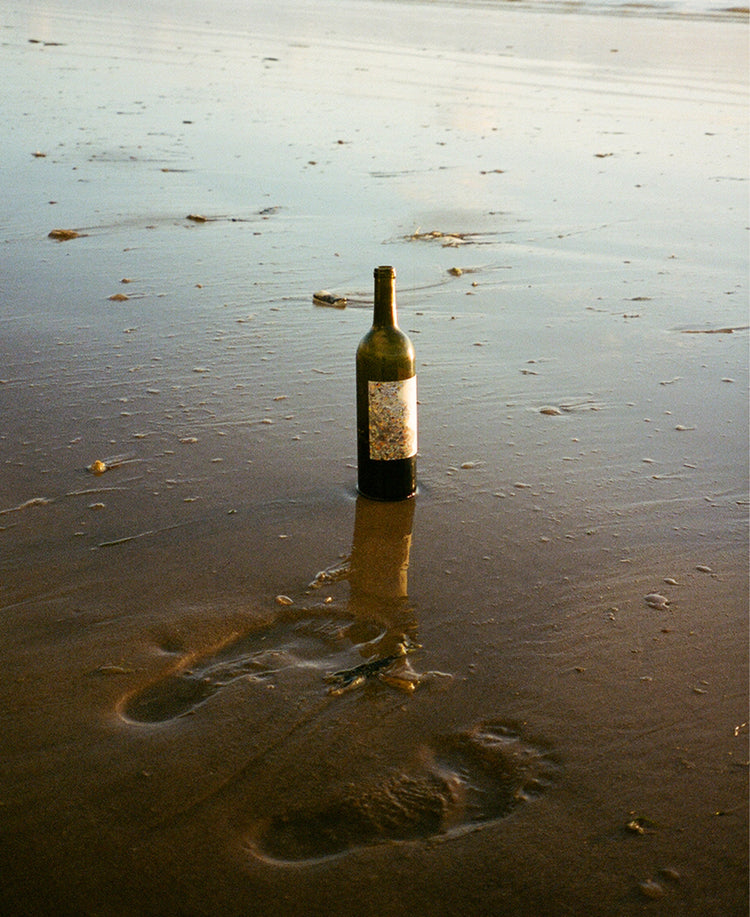 Another Shore red wine on the beach next to footprints