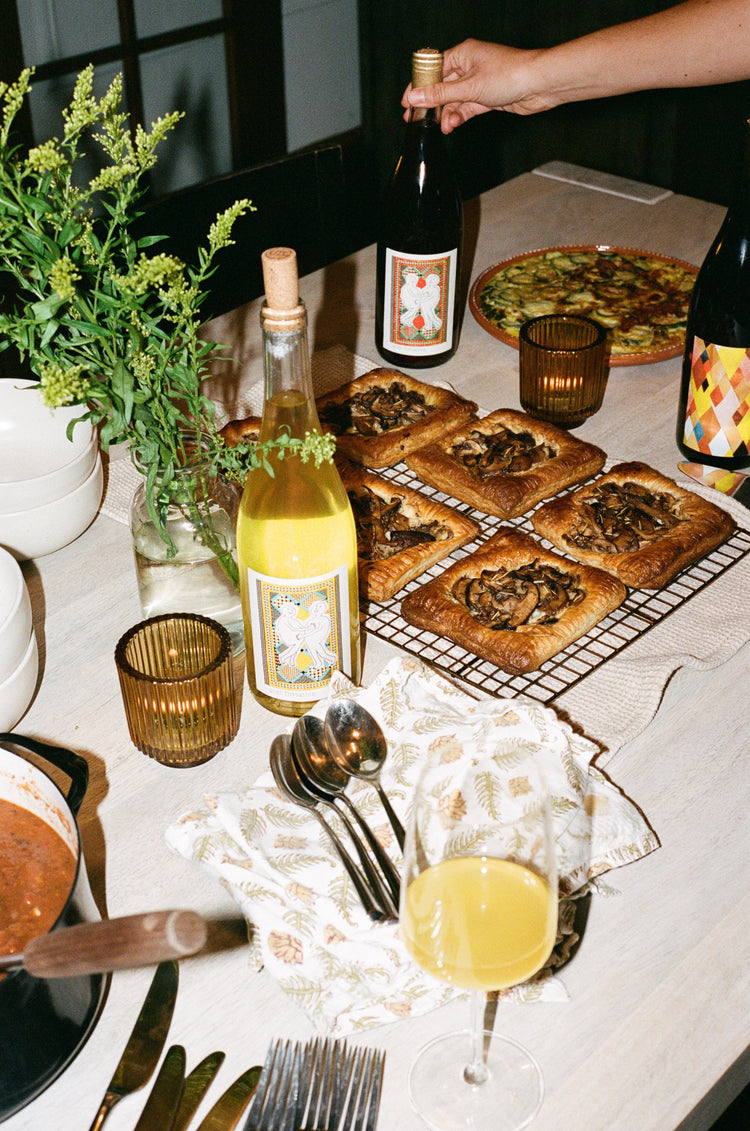 A table with three bottles of wine, silverware, and food.