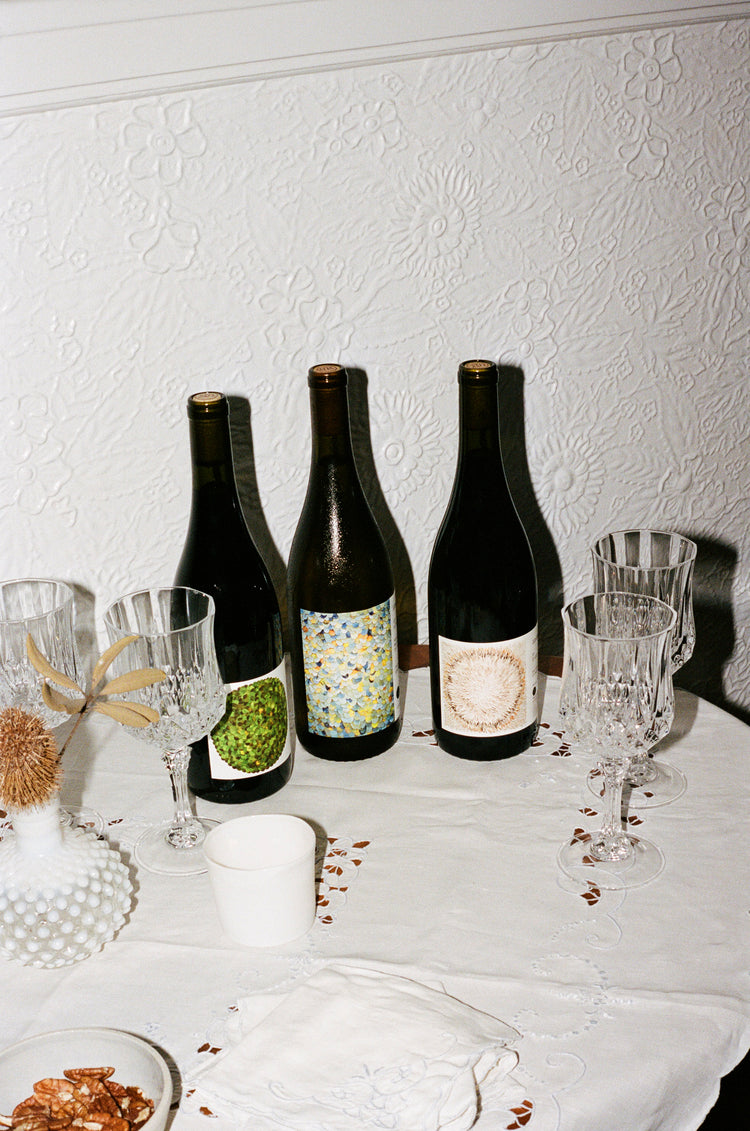 Three unopened bottles of wine on a table with four empty crystal wine glasses.