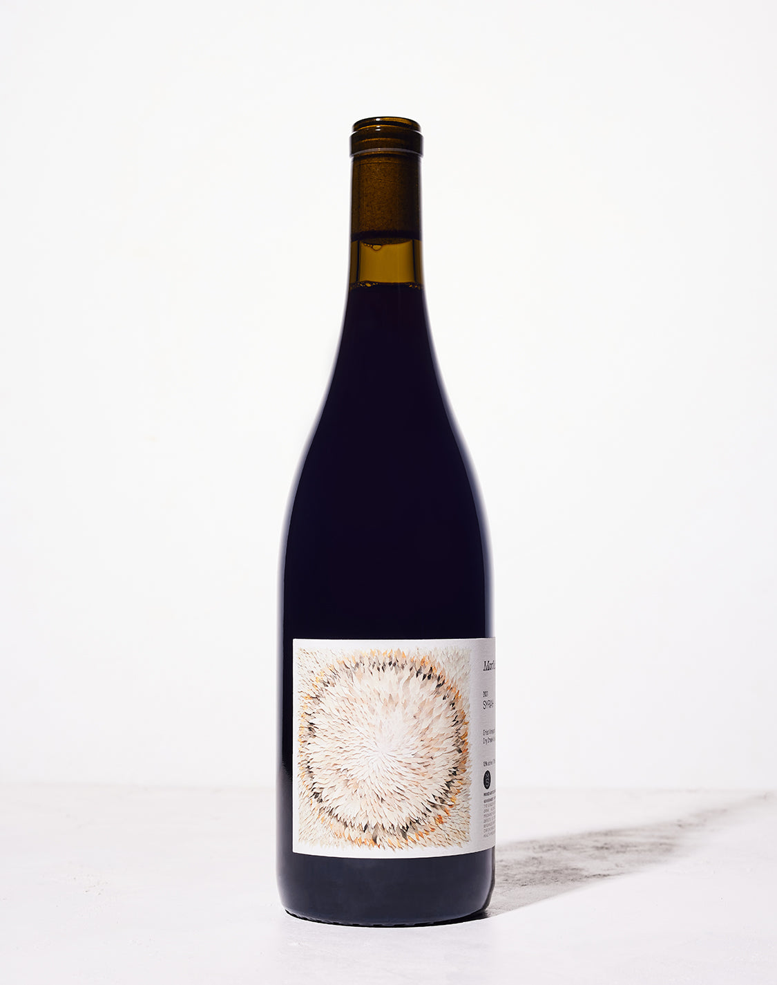 A wine bottle against a white background, featuring a label with an abstract circular pattern of light and dark brown brush strokes. Simple and elegant design.