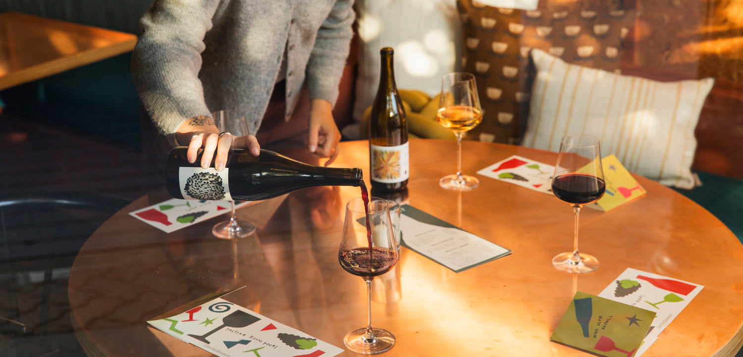 Person pouring wine into a glass on a table with menu cards and a bottle of wine.