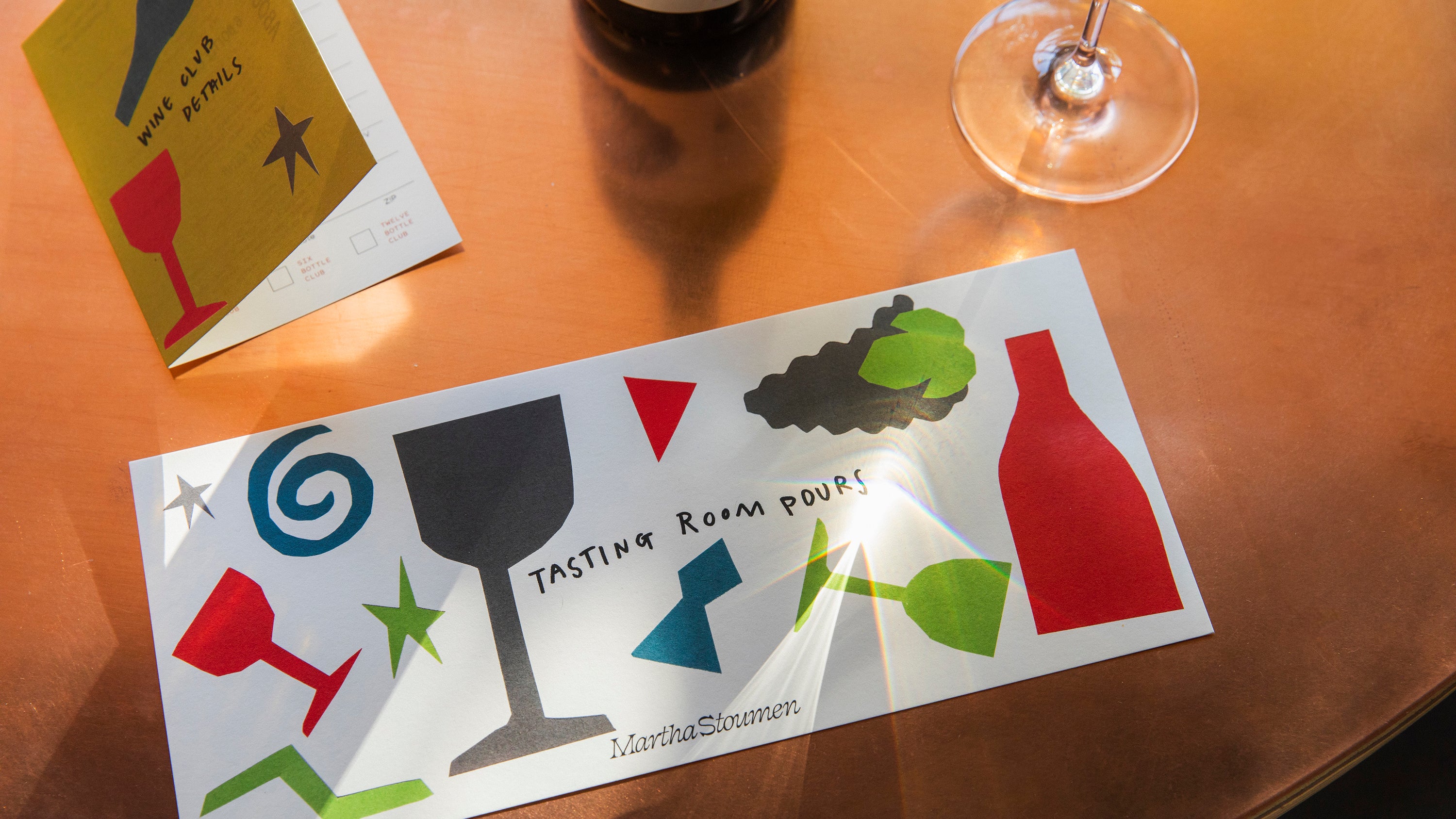 A colorful menu of tasting room pours sits atop a warm copper table and a glass of wine.