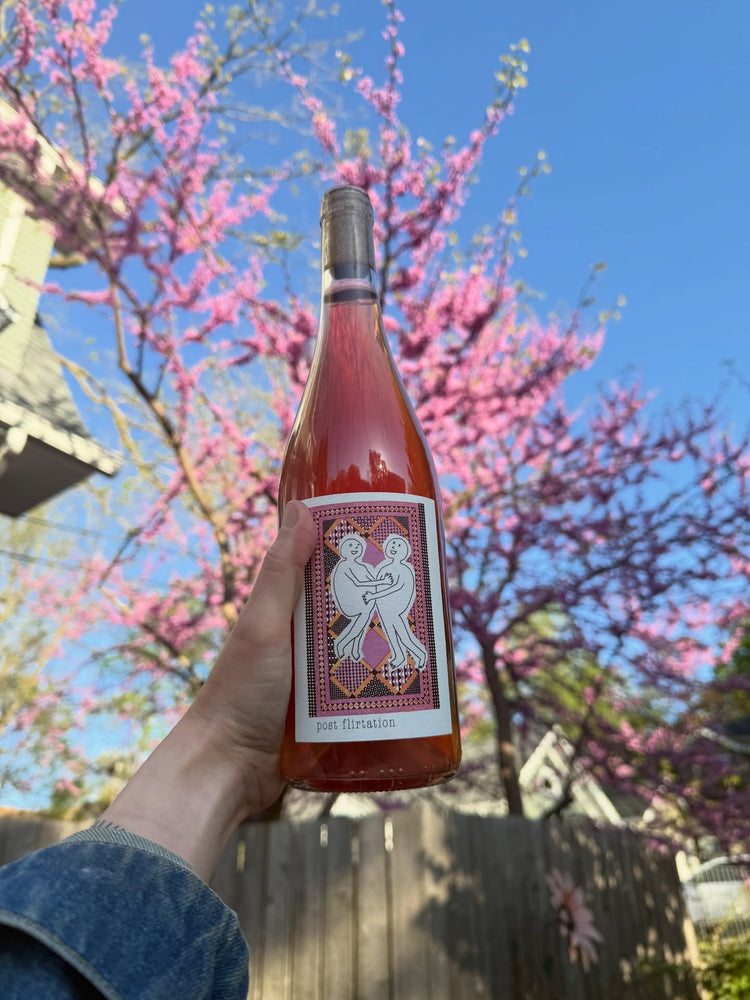Bottle of rosé wine with a decorative label held in front of a flowering tree