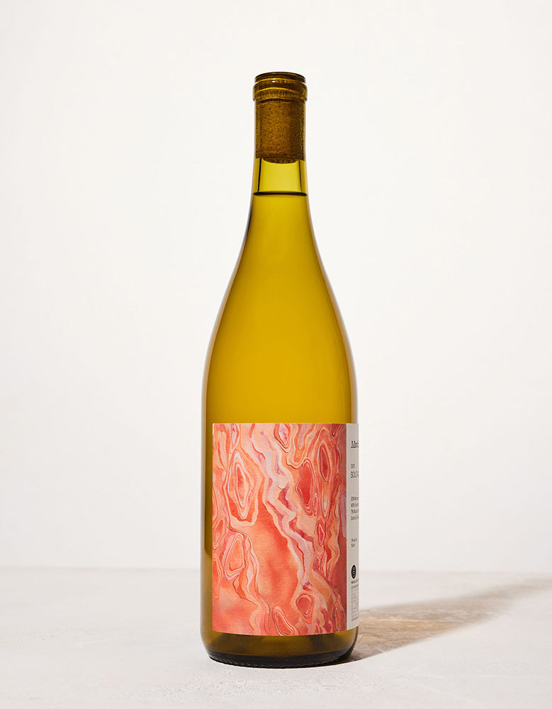 A wine bottle with a cork top, featuring an abstract orange and pink marbled label. It stands against a minimalist off-white background.