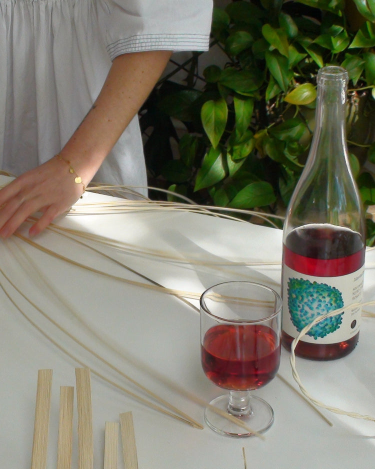 Person working on a decorative item at a table with a bottle and glass of rosé wine.

