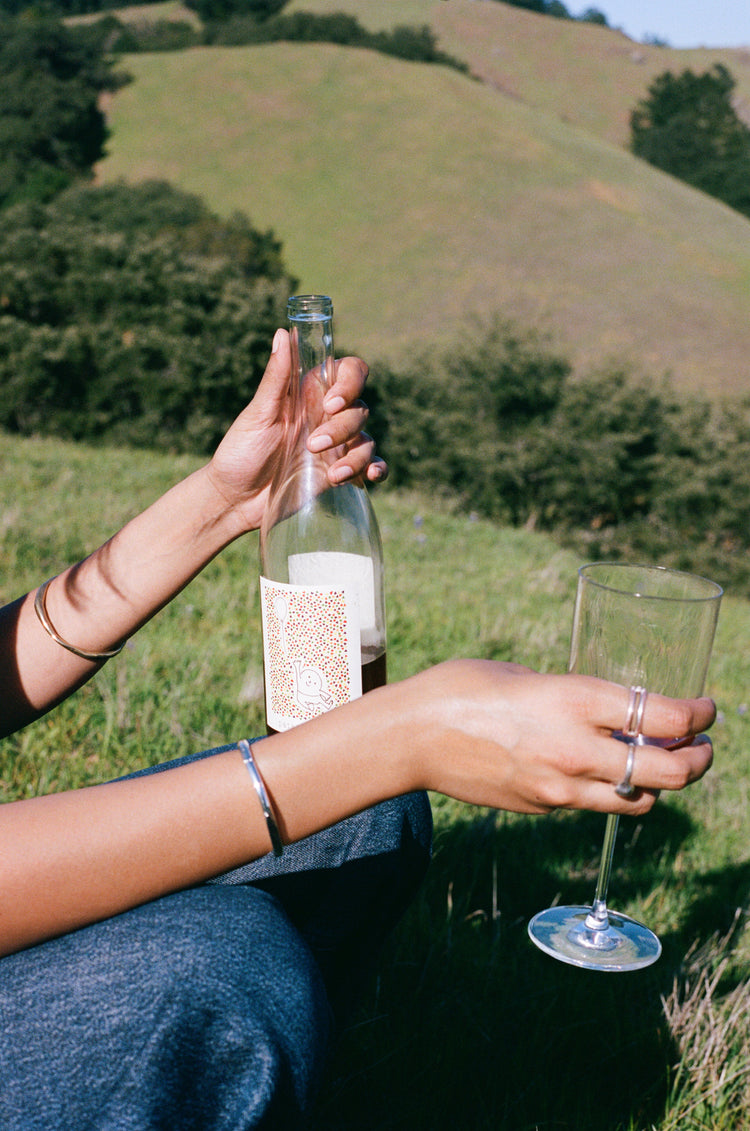 Person holding a bottle and a glass in a grassy outdoor setting