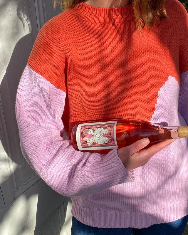 Person wearing a colorful sweater holding a bottle of rose wine.