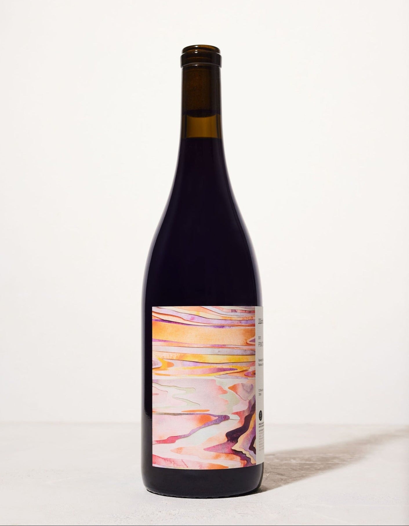 A wine bottle stands against a light background. The label features an abstract design with warm pink, orange, and purple swirls, evoking a serene sunset.