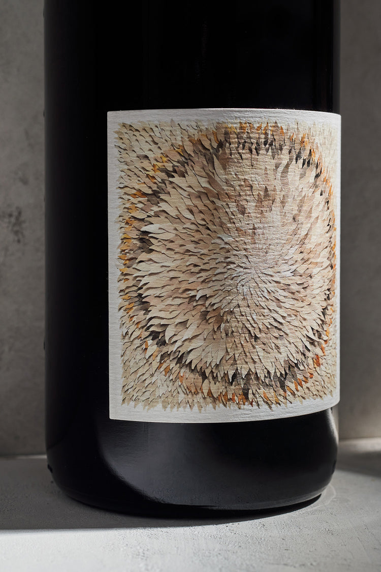Close-up of a wine bottle label with a textured circular pattern of overlapping feathers in earthy tones. It conveys an artistic and elegant feel.